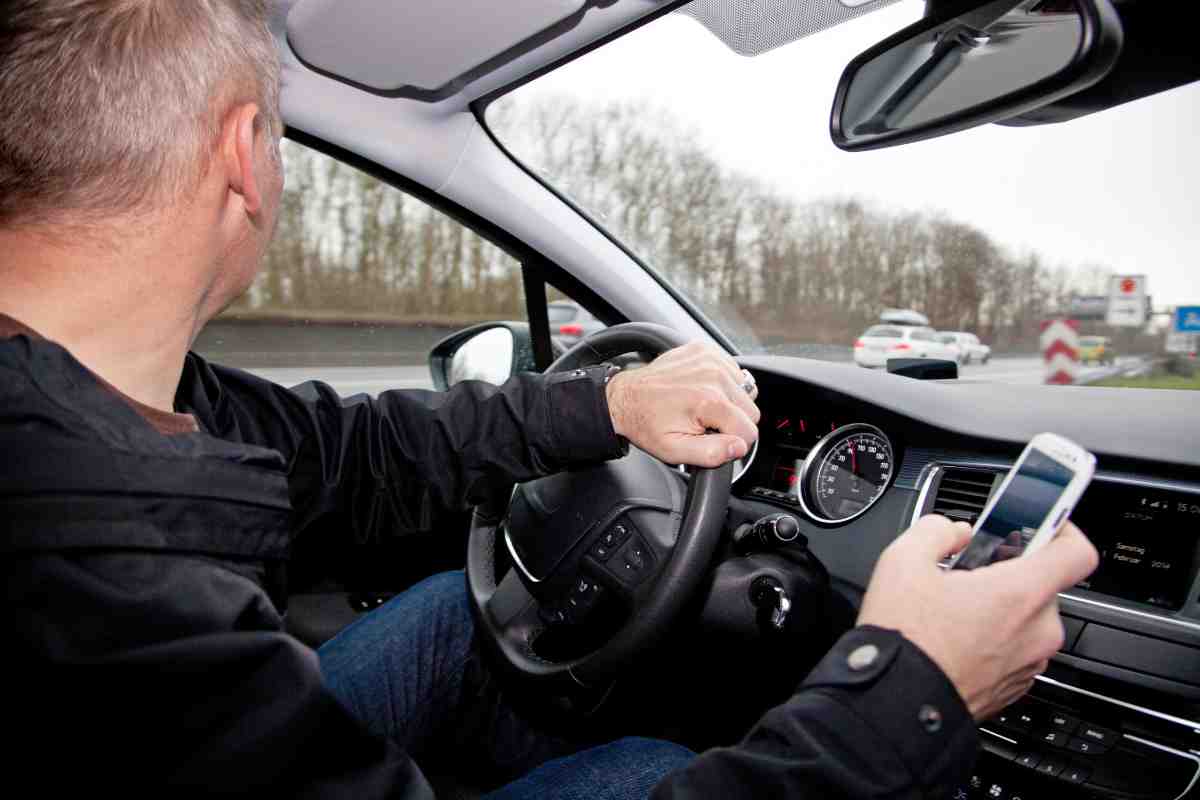 uomo in auto alla guida con cellulare in mano